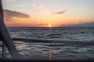 Sunset over the water with the boat railing in the foreground, per the operator caption