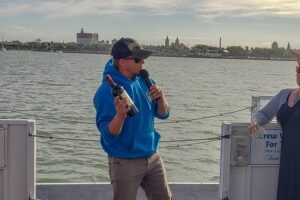 Crew member presenting wine with the St. Augustine waterfront behind
